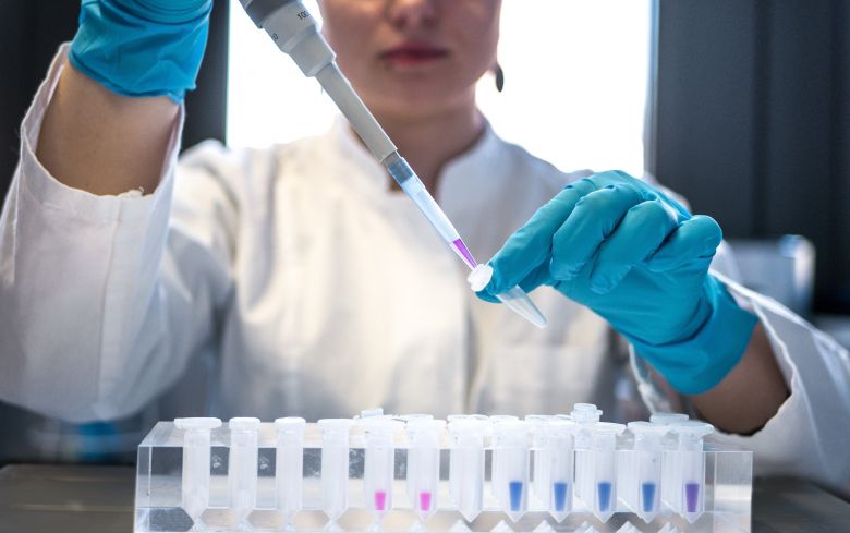 Woman in a lab coat using a pipette to fill test tubes