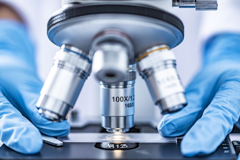 Close-up of blue rubber-gloved hands holding a slide under a microscope. Image: Pixabay